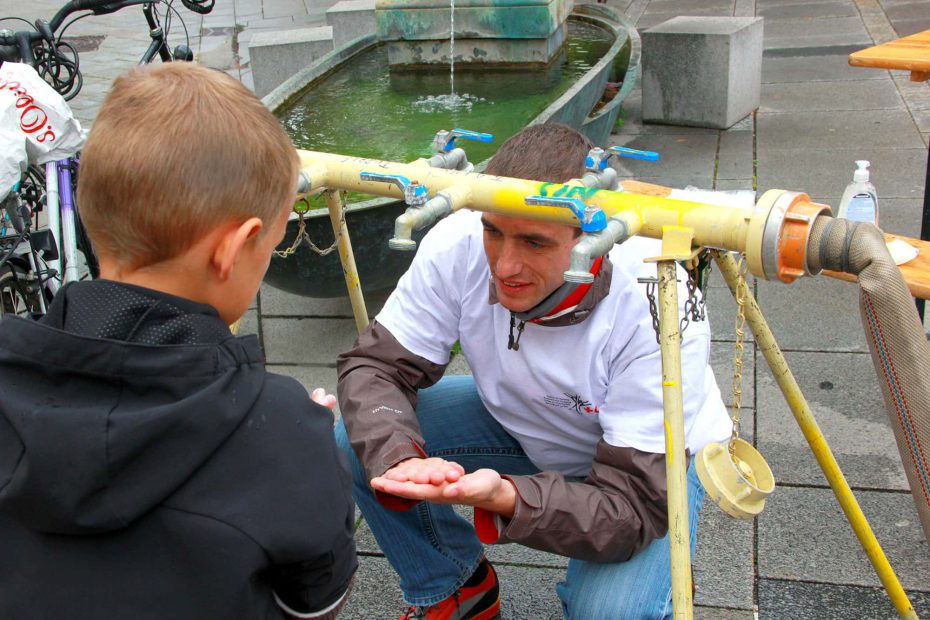 Rotkreuz Mitarbeiter zeigt einem Kind den Wasserverteilerhahn