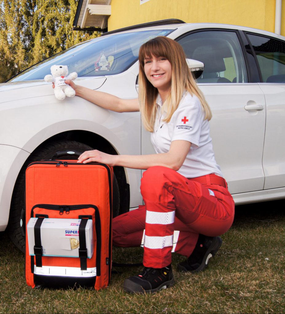 First Responder mit Rucksack kniet vor einem Auto